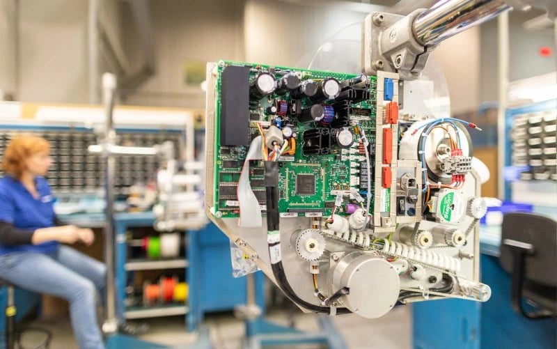 Das Innere einer komplexen Druck- und Etikettiermaschine, die auf die nächste Produktionsstufe wartet, bestehend aus einer PCBA, Motoren, Getrieben, Riemenscheiben und Kabeln.