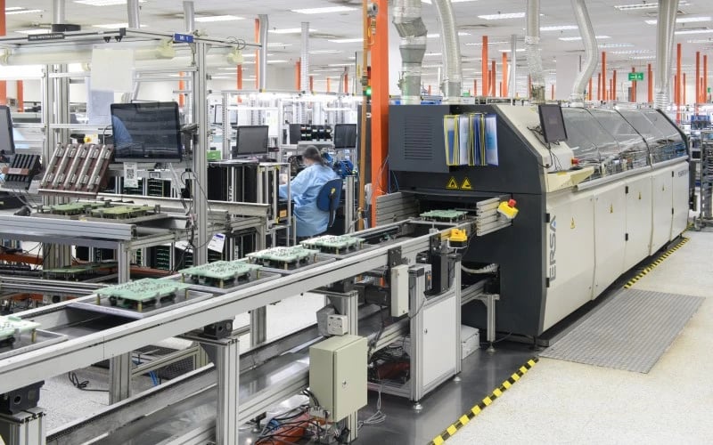 A section of an electronics manufacturing services shop floor showing a selective solder machine with several PCBs lined up waiting to go inside. 