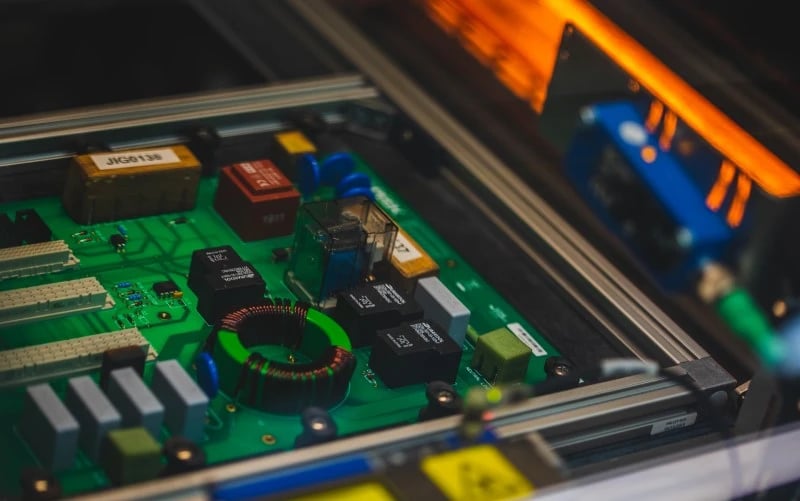 A close up of a green PCBA with through-hole components including coils and relays waiting to go through a selective soldering machine. 