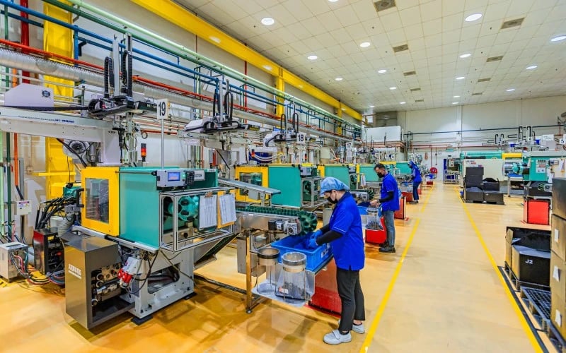 The inside of a plastic injection moulding factory with multiple industrial machines and production operatives on view.