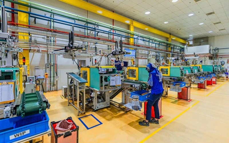 Eine Reihe industrieller Kunststoff-Spritzgiessmaschinen mit einem Produktionsmitarbeiter an der Linie.  