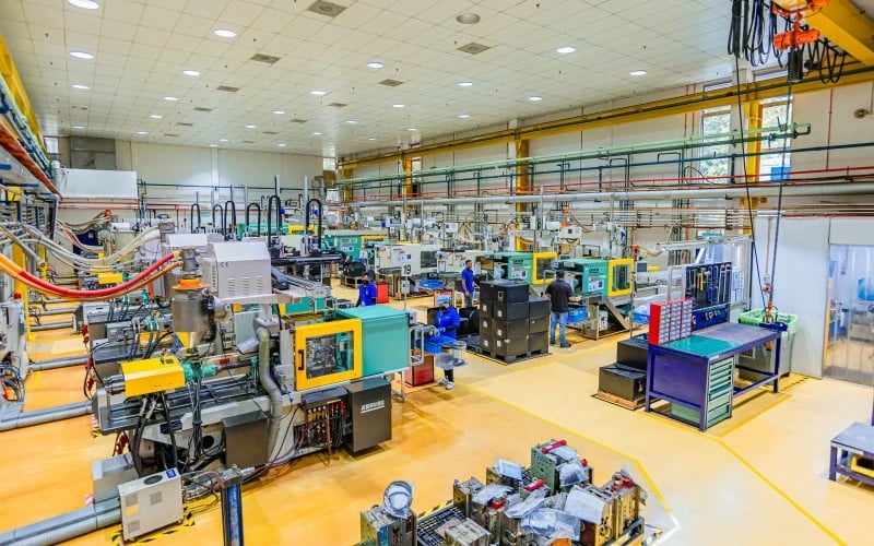The inside of a plastic injection moulding factory with multiple industrial machines and production operatives on view.