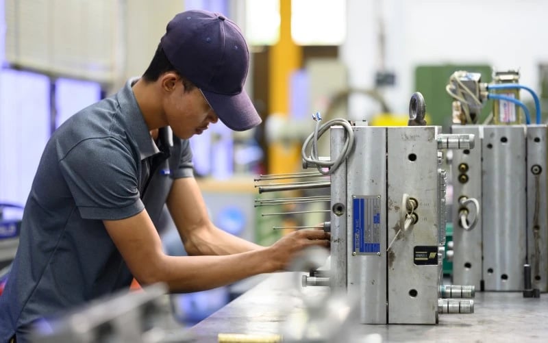 Ein männlicher Produktionsmitarbeiter mit Baseballmütze arbeitet an der Wartung eines grossen und schweren Kunststoff-Spritzguss-Metallwerkzeugs auf einer industriellen Wartungsbank.