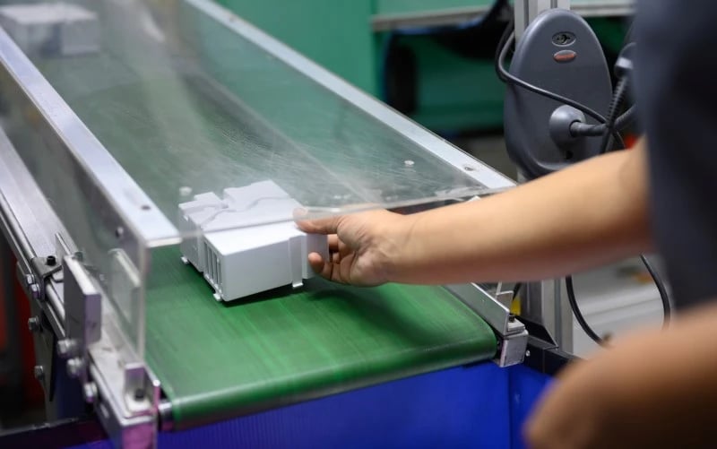 The hand of a production operator removing a completed white plastic part from the end of a plastic injection moulding production line.