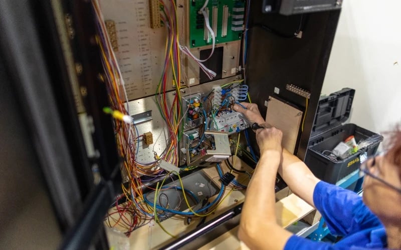 A female production operative wiring various connections together inside an electrical control cabinet.  