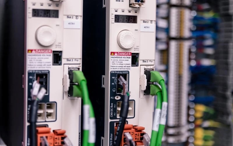 A close up image of two white high voltage circuit breakers with green and black wires plugged in fitted inside a much larger electrical control cabinet.