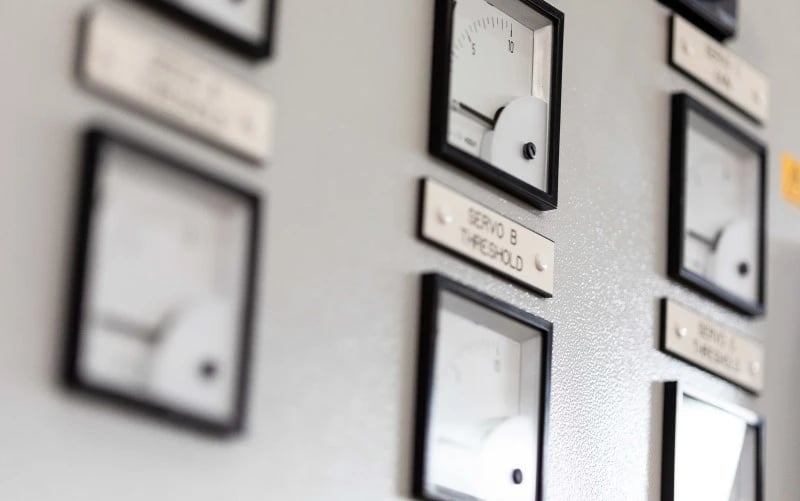 A close up of multiple sensor gauges attached to the front of a large white electrical control cabinet.