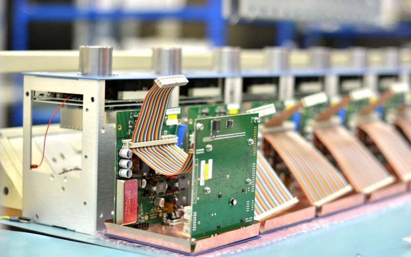 A row of part-built gas measurement desktop machines consisting of multiple green PCBAs, cable assemblies and precision metalwork waiting for the next stage of assembly.