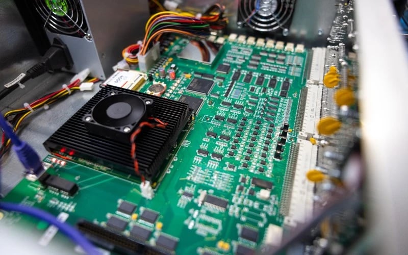 Eine Nahaufnahme einer grünen PCBA, die aus vielen Halbleitern und Drähten besteht, zusammen mit einem grossen schwarzen Kühlkörper und einer Lüftereinheit.  