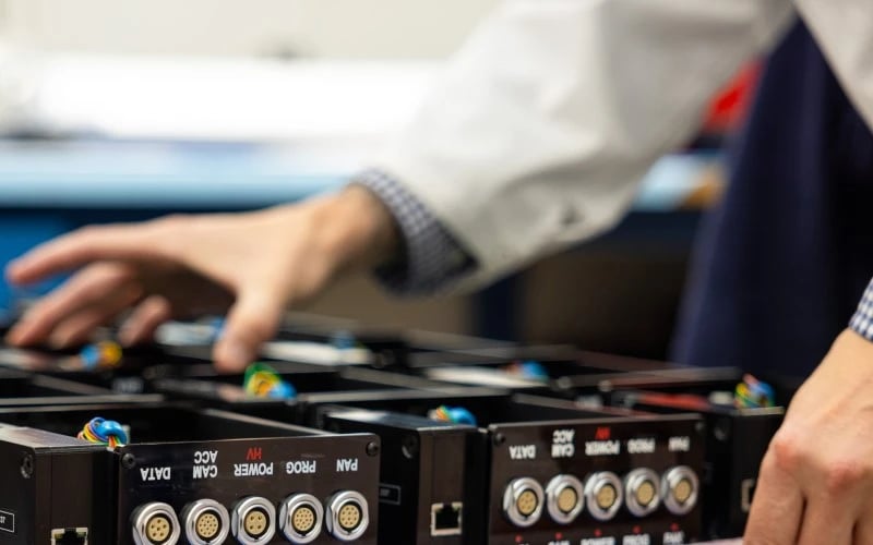 A close up image of a man picking up a black metal enclosure with five connector ports on the back.